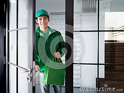 Asian handsome delivery man holding shopping paper bag and opening door to send food or product order by express service to Stock Photo