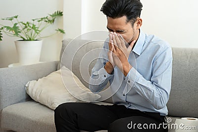 Asian handsome of man having flu season and sneeze using paper tissues sitting on a sofa at home, Health and illness concepts Stock Photo