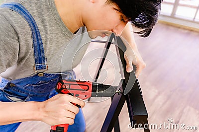 Asian handyman assembling steel table using cordless screwdriver driving screw fix Stock Photo