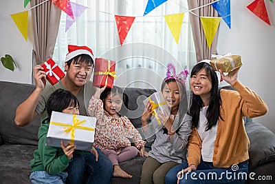 Asian Happy family with daughter in Santa hats gathered together on Christmas time and enjoy gifts box Stock Photo