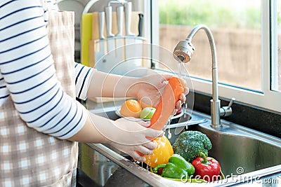 Asian healthy woman washing an carrot and other fvegetable above kitchen sink and cleaning a fruit / vegetable with water to Stock Photo