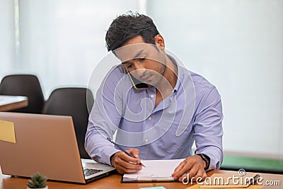 Asian indian business man talking with customer on mobile phone to get requirement and sale support holding pen Stock Photo