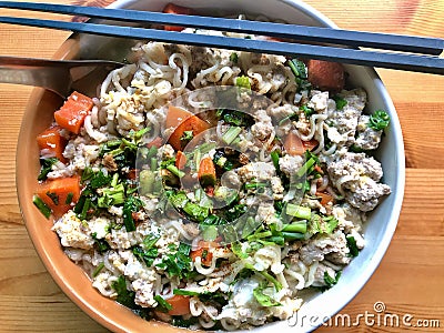 Asian instant noodle with fresh pork chop carrot coriander and spring onion in clay round boil on wood background Stock Photo
