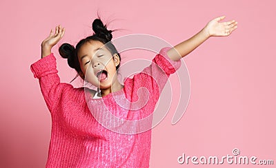 Asian kid girl in pink sweater, white pants and funny buns sings singing dancing on pink Stock Photo