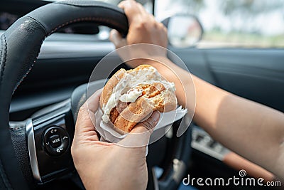 Asian lady holding hamburger to eat in car, dangerous and risk an accident Stock Photo