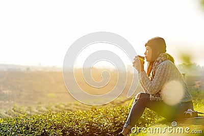 Asian lifestyle women wearing sweater, sitting and drinking hot coffee or tea relax outdoor in the sunrise morning sunny day at te Stock Photo