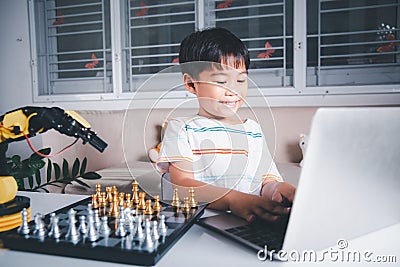 Asian little boy programming code to robot machine arm on laptop for play chess Stock Photo