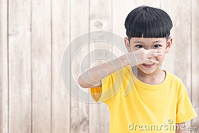 Asian little child covers nose with hand showing that something stinks with wood wall background Stock Photo