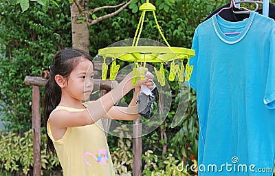 Asian little child girl putting clothespin and hangs socks to dry a clothes. Kid doing laundry in the garden Stock Photo