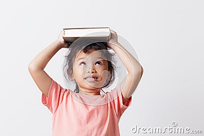 Asian little girl holding a book on head and eyes looking top on white background head. On face a cute girl so happy and smile Stock Photo