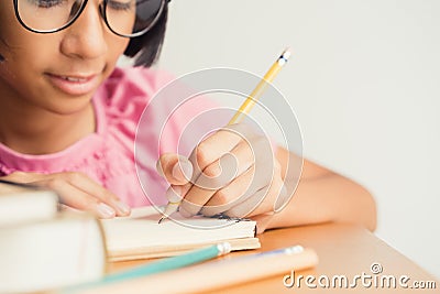 Asian little girl wears glasses while sit writing on desk at her home Stock Photo