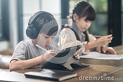 Asian little young children self learning at home. The boy using tablet and headphones for E-learning at home. The girl doing home Stock Photo