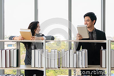 Asian male and cuacasian female university students standing at bookshelf seaching and reading book in library Stock Photo