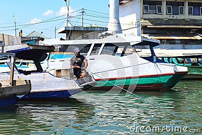 Asian male parking his boat over the sea, fisherman resting his wooden boat at the port or harbor area Editorial Stock Photo