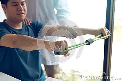 Asian male physical therapist descent working with patient doing stretching exercise with a flexible exercise band in clinic room Stock Photo