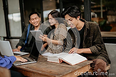 Asian male student reading a thick book while doing coursework Stock Photo