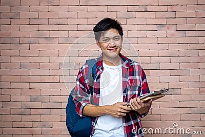 Asian male students wear plaid shirts. Standing next to a brick wall, carrying a backpack, carrying books, school supplies, Stock Photo