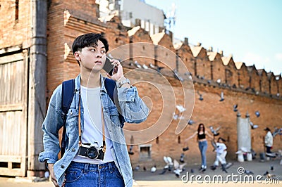 Asian male traveler talking on the phone, calling someone while standing at Tha-Phae gate Editorial Stock Photo