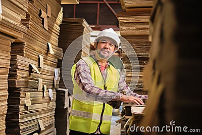 Asian male worker in uniform inspects with laptop at paper factory warehouse Stock Photo