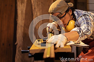 Asian man Carpenter wearing PPE working use measuring tape on timber for marking woodwork furniture in carpentry workshop Stock Photo