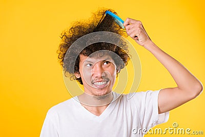 Asian man combing curly hair on yellow background Stock Photo