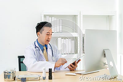 Asian man doctor wears white coat and headset speaking videoconferencing on laptop computer using online video call consultation Stock Photo