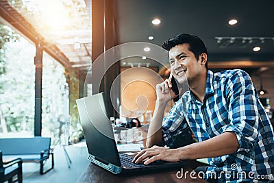 Asian man freelance work on computer touch pad while talking on smart phone With a happy smile, young business man use laptop Stock Photo