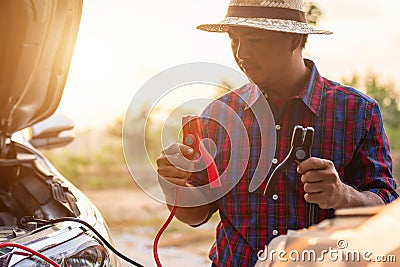 Asian man holding black and red battery cable and trying to connect the cable to his car Stock Photo