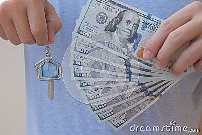 Asian man holding one hundred dollar bills and home shape key chain. Property investment and mortgage finance concept Stock Photo