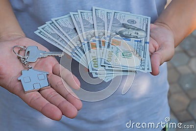 Asian man holding one hundred dollar bills and home shape key chain. Property investment and mortgage finance concept Stock Photo