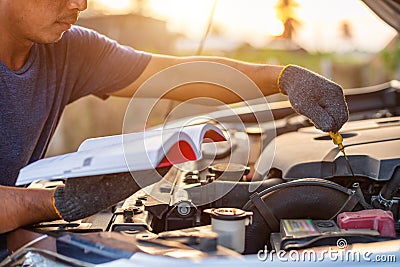 Asian man holding and reading the car user manual or user instruction to checking or fixing engine of modern car Stock Photo