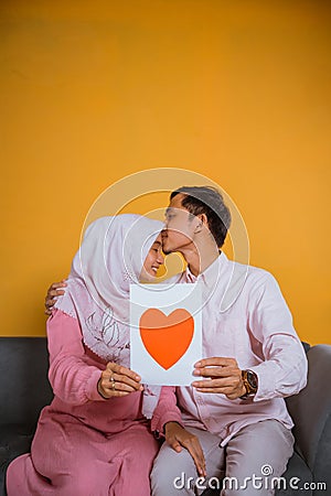 Asian man kisses hijab woman showing a paper love drawing Stock Photo