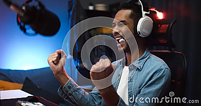 Asian man playing online computer video game, colorful lighting broadcast streaming live at home. Ecstatic celebration winning a m Stock Photo