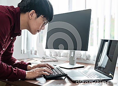 Asian man programmer looking on screen laptop to typing code data with keyboard about website and applications Stock Photo