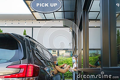 Asian man in protective mask taking food bag and coffee with woman waitress wearing face mask and face shield at drive thru during Stock Photo