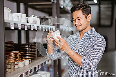 Asian man shop owner holding ceramic cup from shelf Stock Photo