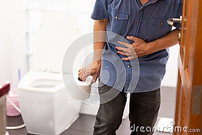 Asian man suffers from diarrhea holding tissue roll or toilet paper near a toilet bowl,man have abdominal pain,stomachache, Stock Photo