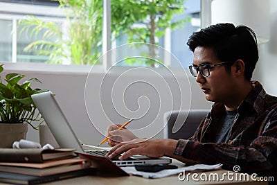 Asian man using laptop computer and counting taxes or house expenditures Stock Photo