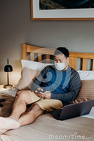 Asian man weared medical mask. Sitting and using cell phone in bedroom Stock Photo