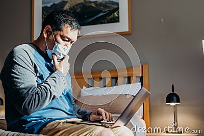 Asian man weared medical mask. Sitting and using laptop in bedroom Stock Photo