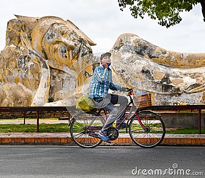 Mask wearing man cycling infront of Buddha statue Editorial Stock Photo