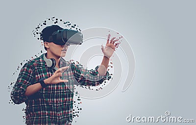 Asian man wearing glasses of virtual reality dissolving into pixels is touching on gray background Future Technology Concept Stock Photo