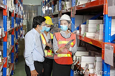 Asian manager talking to employees wearing facial mask and safety vest working in warehouse checking for the inventory Stock Photo