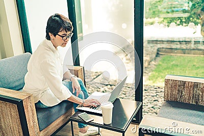 Asian mature woman using laptop with smartphone and coffee at cafe, vintage tone, middle aged adult with modern gadget technology Stock Photo