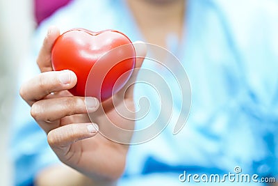 Asian middle-aged lady woman patient holding red heart in her hand with bright face on wheelchair in nursing hospital ward Stock Photo