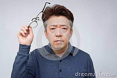 Asian middle-aged male trying to take off glasses and see something. poor sight, presbyopia, myopia Stock Photo