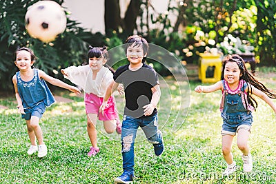 Asian and mixed race happy young kids running playing football together in garden. Multi-ethnic children group, outdoor exercising Stock Photo