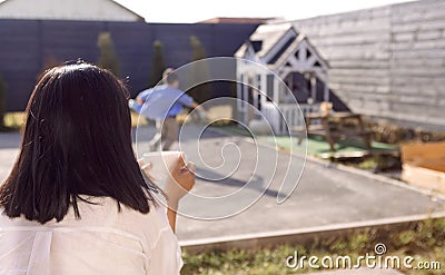 Asian mom holds a cup and drinks tea in the backyard of the house. A young woman looks after her son in the garden Stock Photo