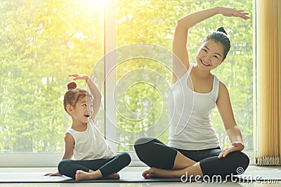 Asian mom practice yoga at home with a adorable daughter sitting next to her, trying to imitate the mother`s posture Stock Photo