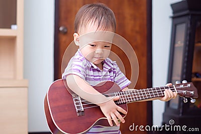 Asian 18 months / 1 year old baby boy child hold & play Hawaiian guitar or ukulele Stock Photo